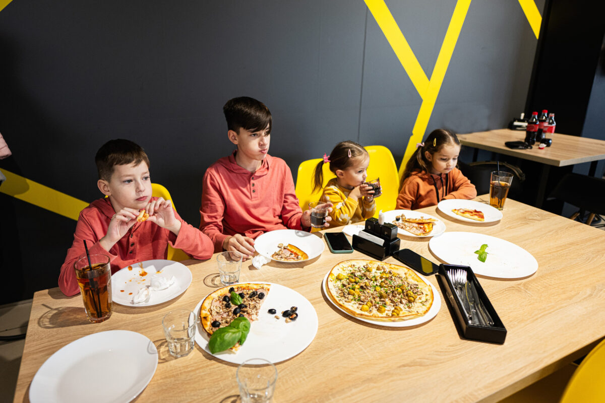 Four kids eating italian pizza in pizzeria. Children eat at cafe.