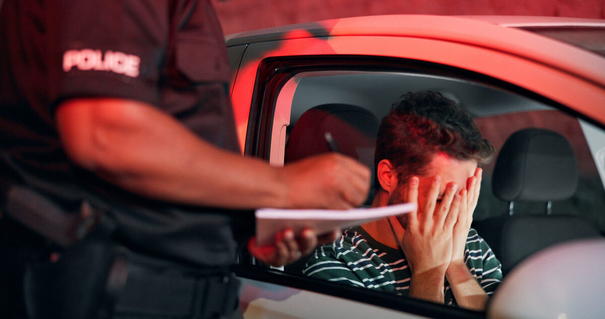 Traffic stop, man and crying in car with police, ticket and stress for drunk driving or speeding at night. Travel, transport and driver in vehicle with highway patrol, lights or street compliance
