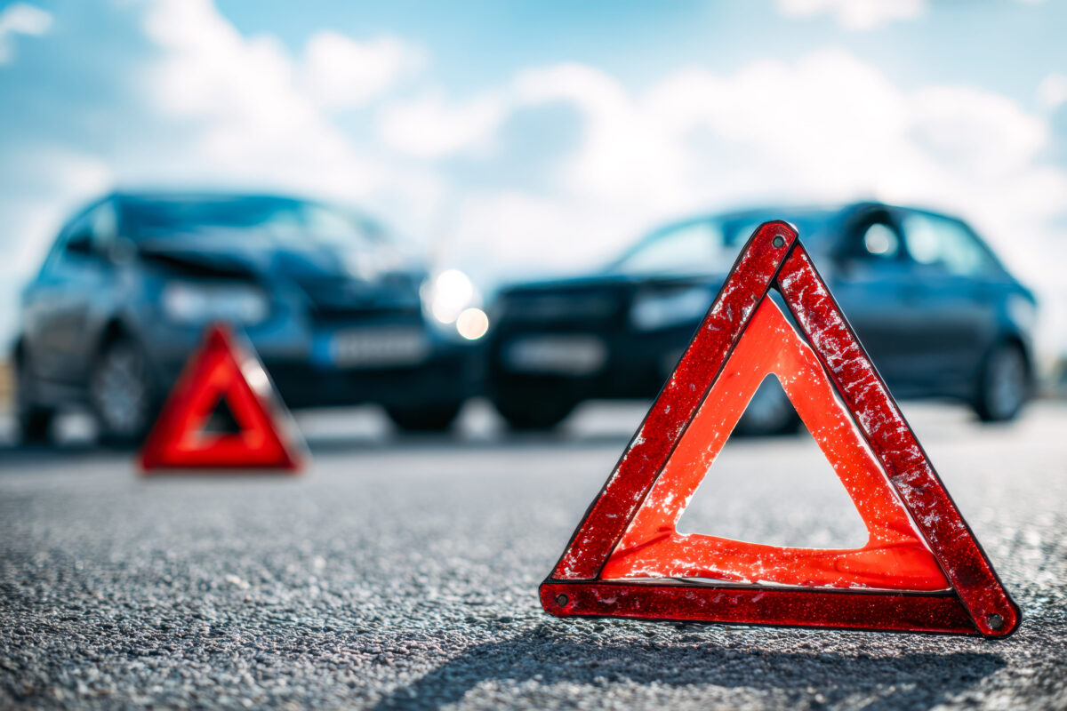 A safety warning triangle stands alert on the asphalt, with orderly parked vehicles lining the roadside behind, conveying caution amid everyday traffic.