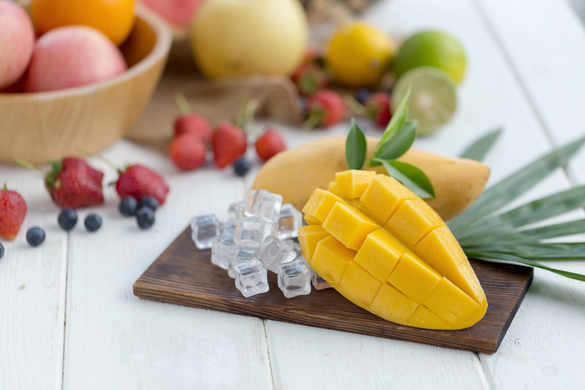 Ripe Mango on a wooden plate with ice cubes and fruit as background.