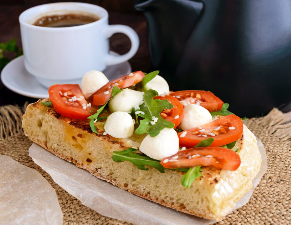 Classic sandwich with mozzarella, fresh tomatoes, arugula and sesame seeds on toast and a cup of coffee. Breakfast.