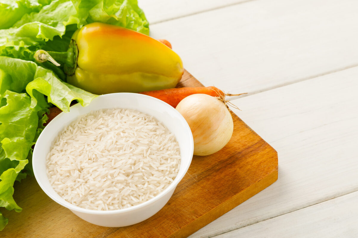 Fresh vegetables with rice in a white ceramic bowl on a wooden cutting board on a white table