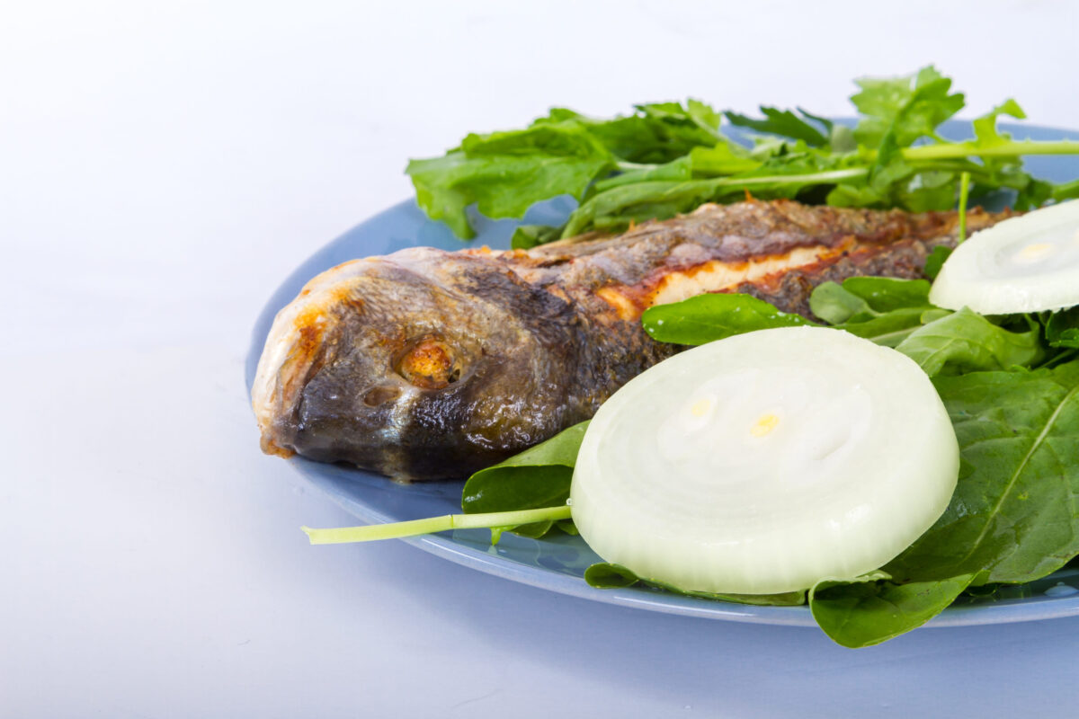 Detailed view of grilled fish, served with green vegetables and onion.