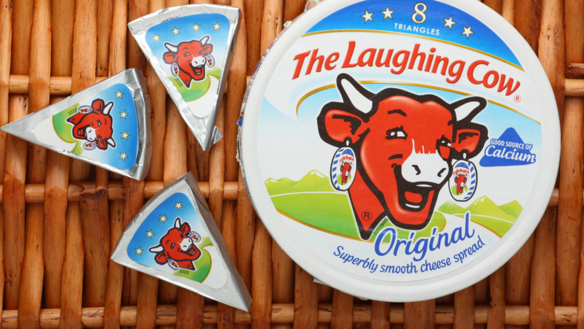 A box of The Laughing Cow Cheese Spread and three portions of foil wrapped cheese on a wicker background