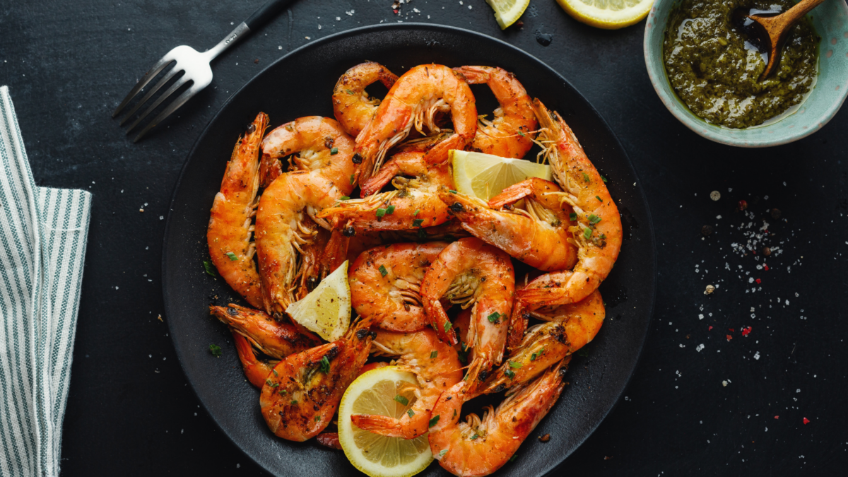 Tasty shrimps with spices and sauce on plate on dark background. Image Credit: nerudol/ Shutterstock
