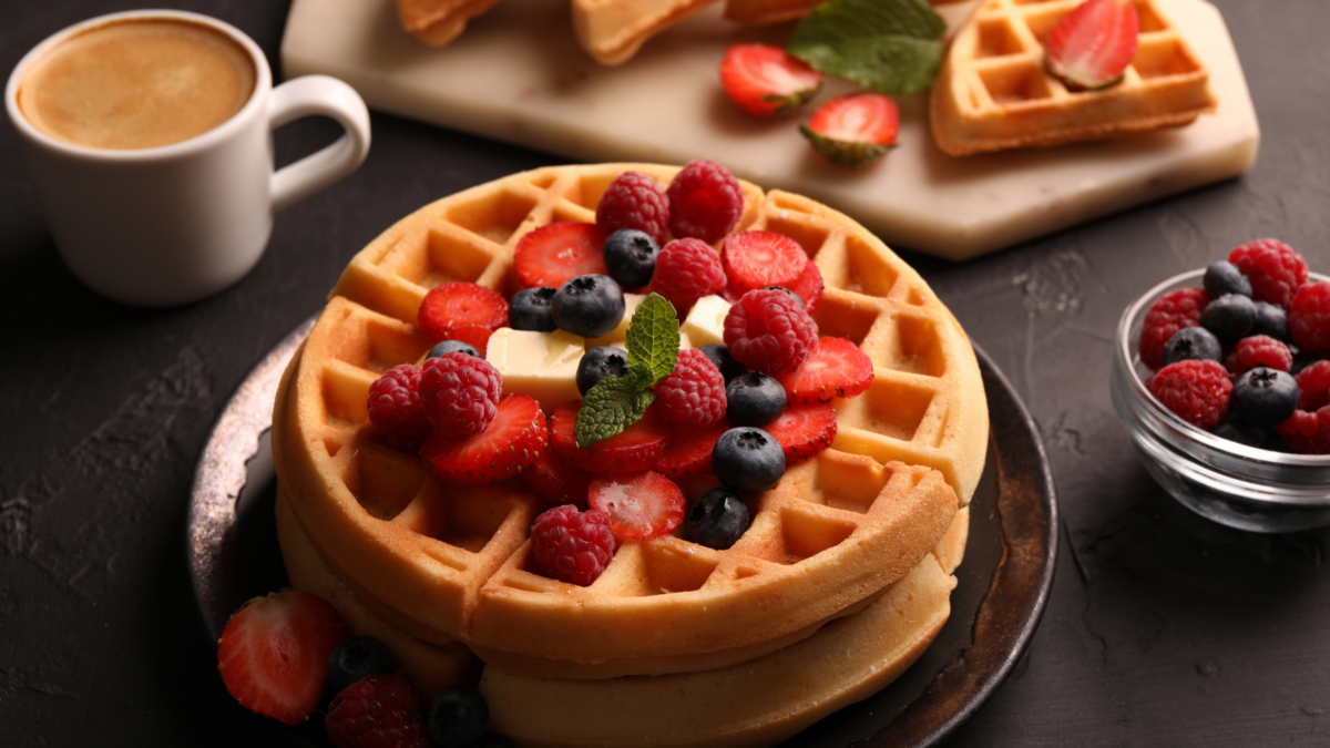 Tasty Belgian waffles with fresh berries, cheese and cup of coffee on black table