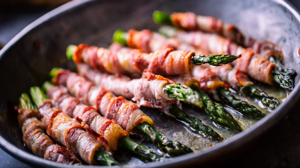 Fried old pan full of rolled bacon with green asparagus