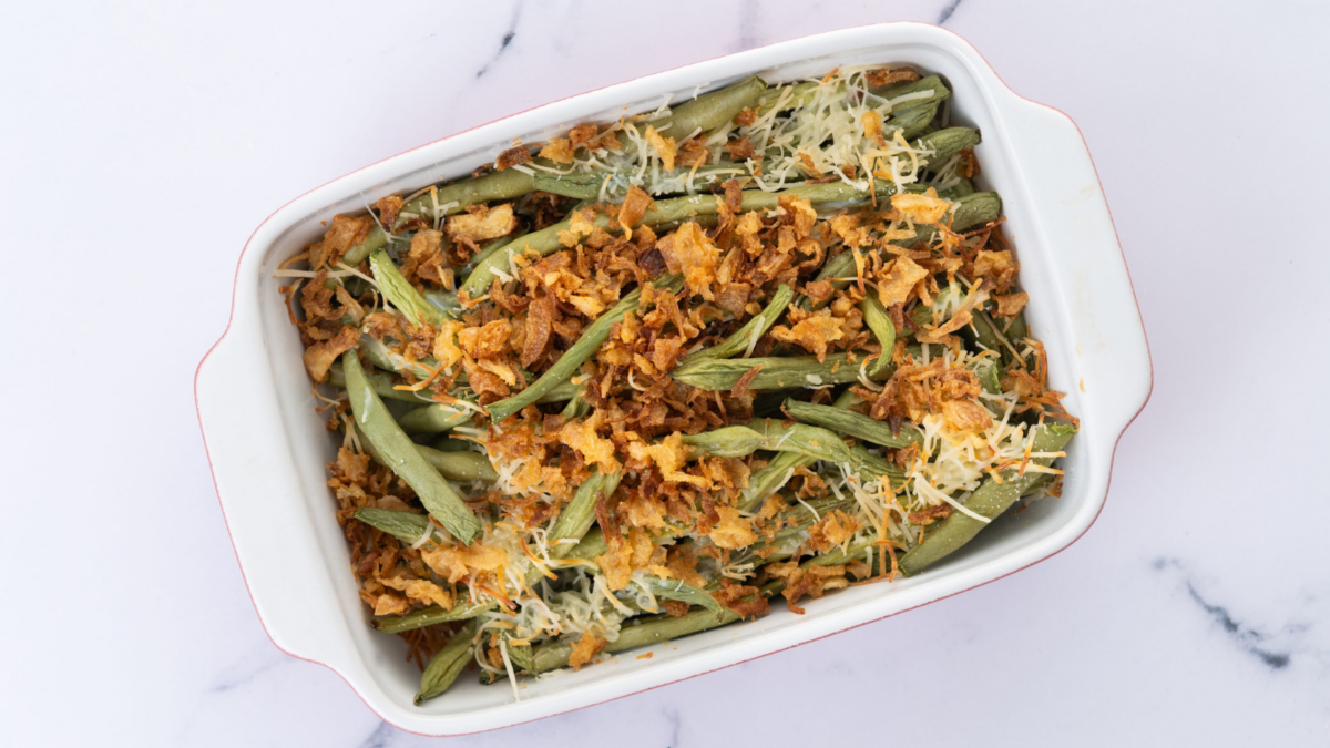 A traditional green bean casserole topped with French Fried Onions and cream of mushroom on white marble
