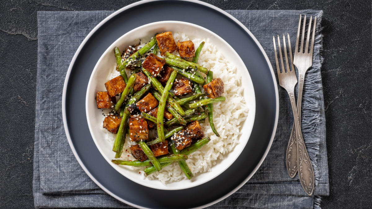 garlic green bean stir fry with crispy tofu served with jasmine rice in white bowl with forks on dark grey concrete table