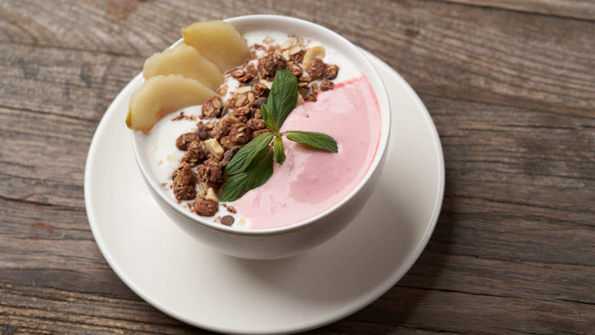 A delicious bowl of creamy yogurt topped with crunchy granola, fresh banana slices, and a sprig of mint, perfect for a refreshing breakfast or snack any time of the day.