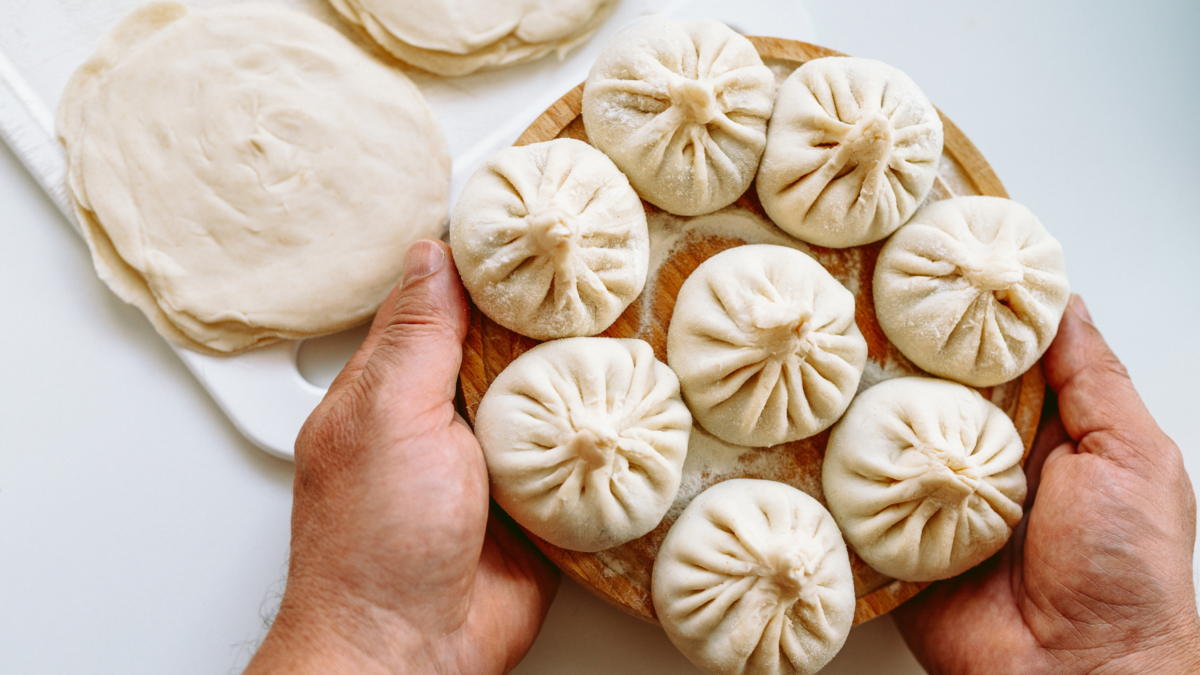 hands cook hold round wooden board with floured, handmade dumplings