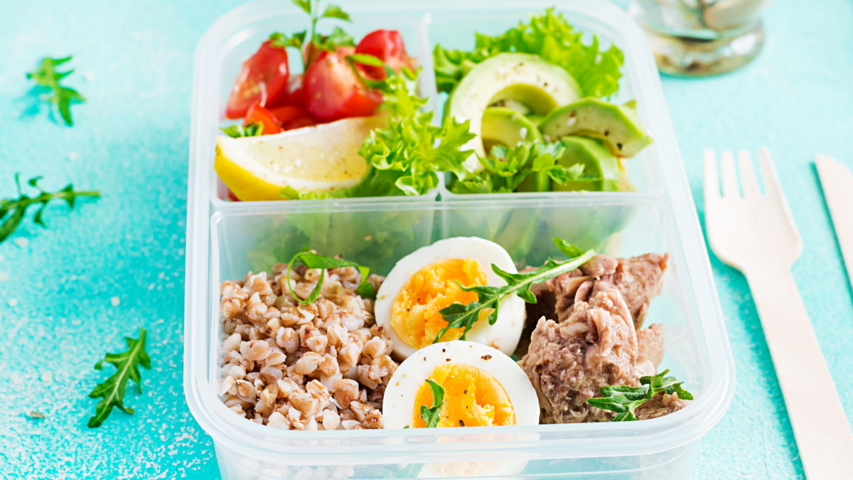 A vibrant lunch box filled with nutritious ingredients, showcasing a delightful assortment of fresh vegetables, hard-boiled eggs, tuna and grains.