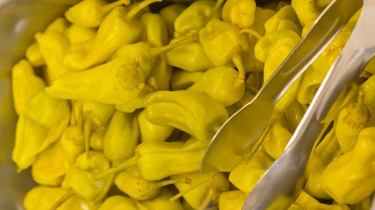 A vibrant assortment of yellow chili peppers awaits in a metal tray, inviting culinary creativity. Perfect for adding a zesty kick to dishes or enjoyed pickled alongside savory meals, these peppers are a staple in many kitchens, promising to spice things up.