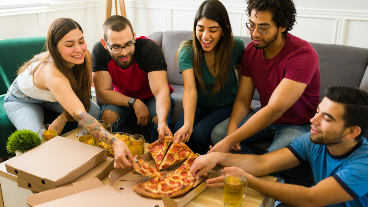 Excited friends eating pepperoni pizza and drinks while having fun together at home