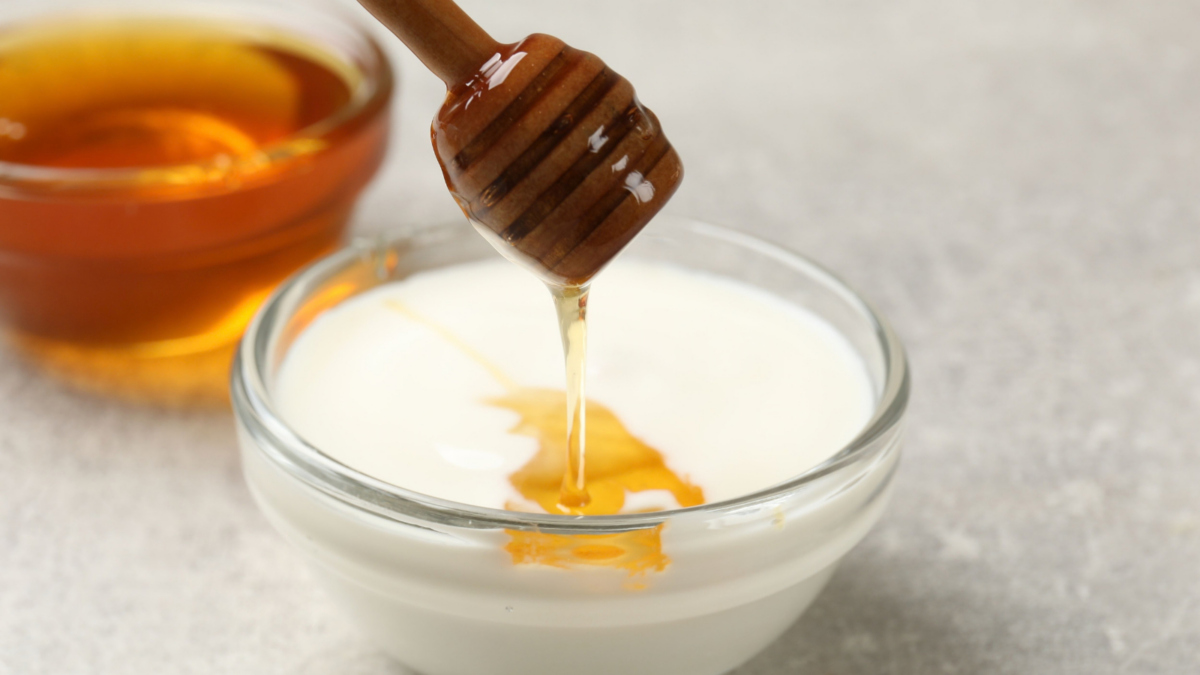 Dripping honey into Greek yogurt at light grey table