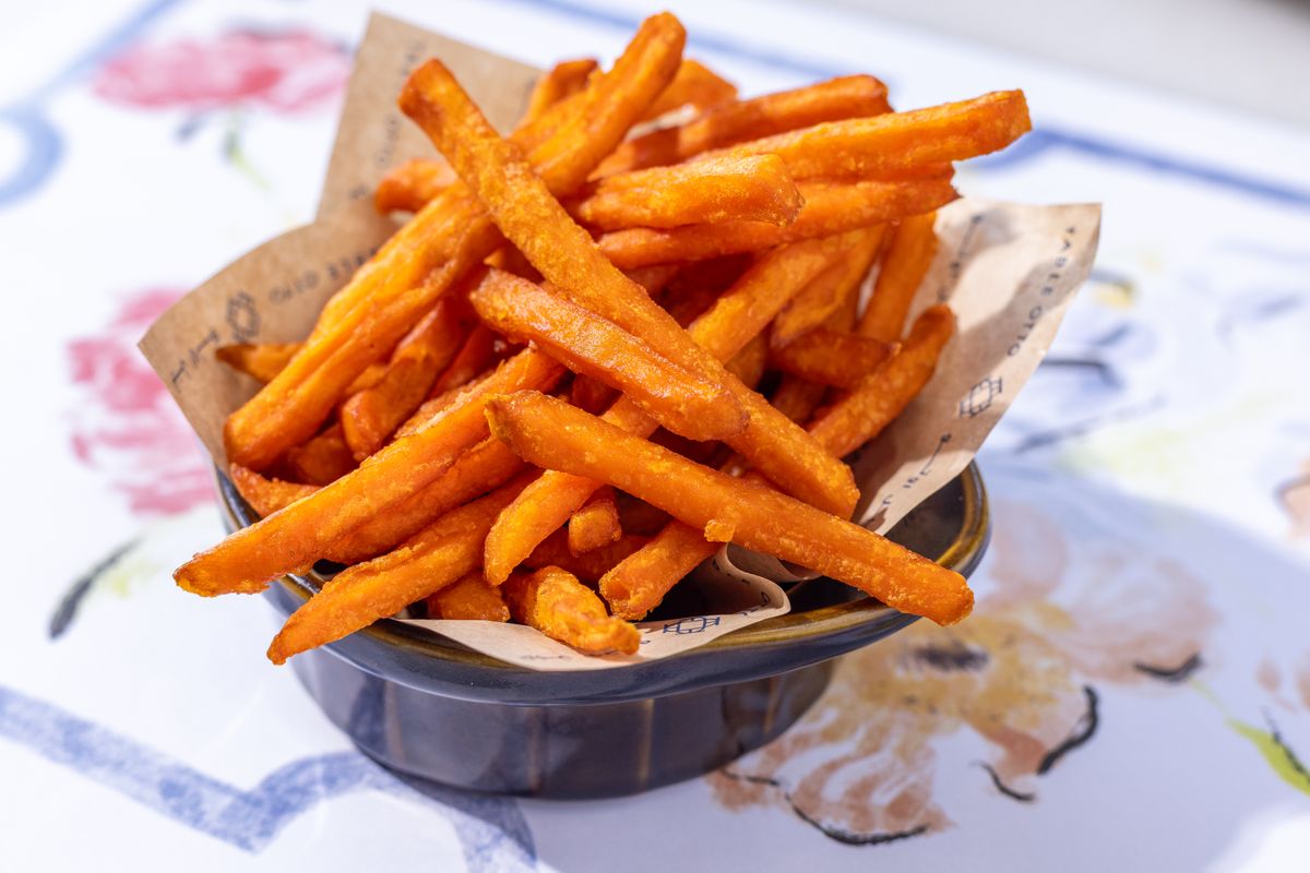 A bowl of crispy sweet potato fries served on an artistic table setting, perfect for food lovers.
