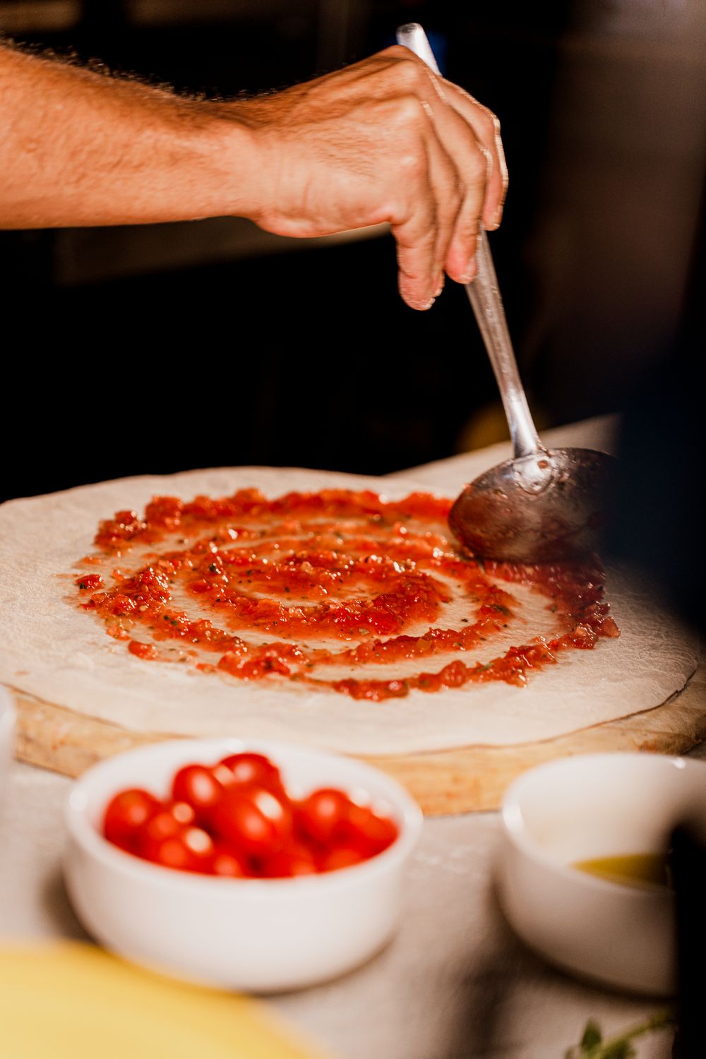 A close-up of a hand spreading tomato sauce on pizza dough, showcasing Italian cuisine preparation.