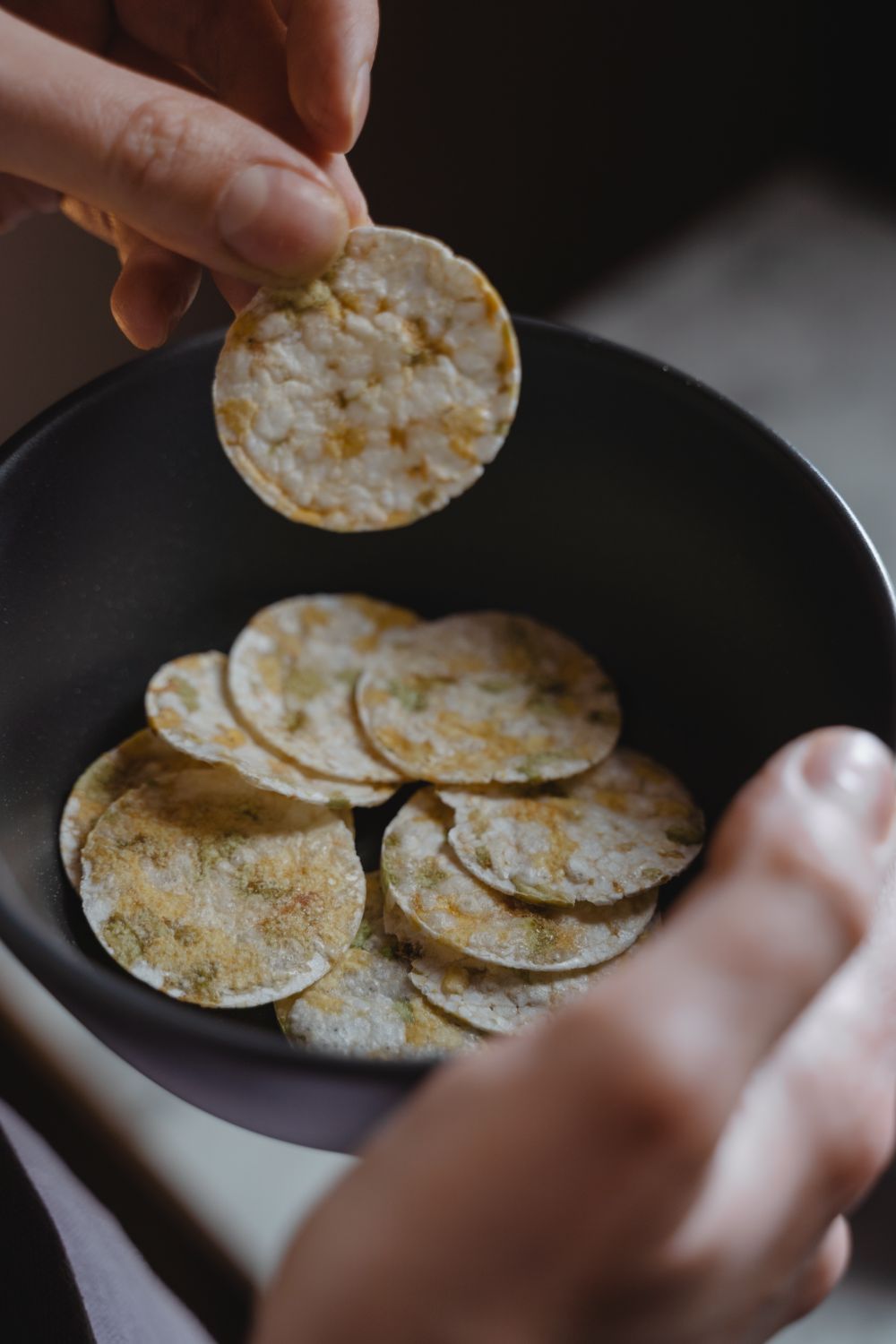 A close-up shot of a person holding a bowl filled with rice crackers in natural lighting.