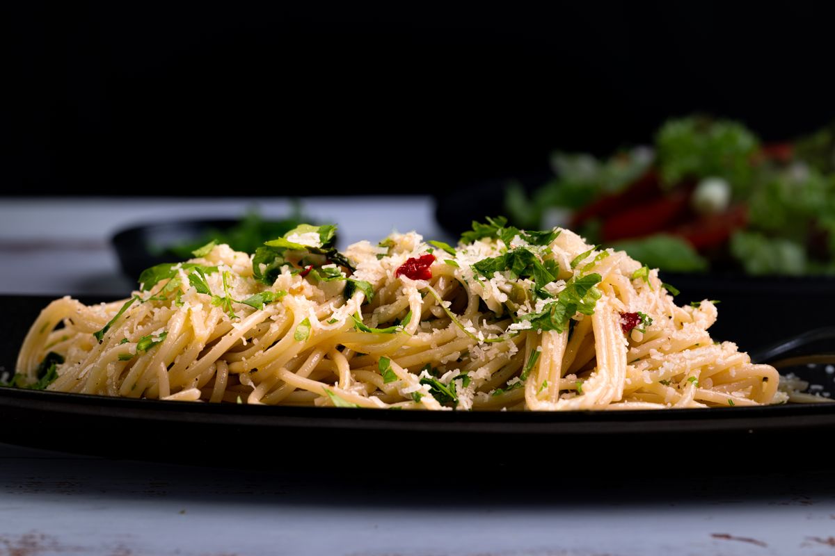 A closeup of a savory spaghetti garnished with fresh herbs and grated cheese.