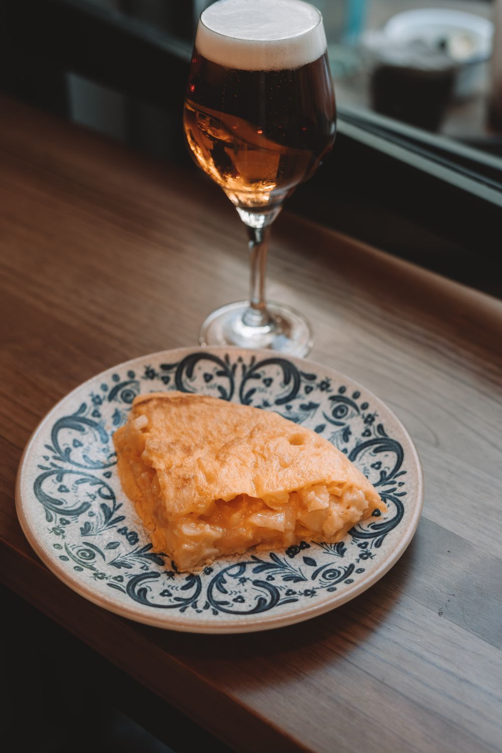 A delicious pastry on a decorative plate accompanied by a beer glass on a wooden table indoors.
