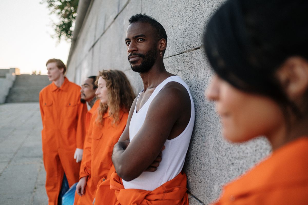 South Korea’s Plan to Provide Airline Meals to Deportees Sparks Debate Among Officials 1 A diverse group of adults in orange uniforms standing against a wall outdoors.
