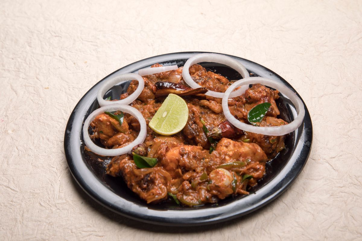 A flavorful Indian chicken dish garnished with onions and lime, perfect for spice lovers.