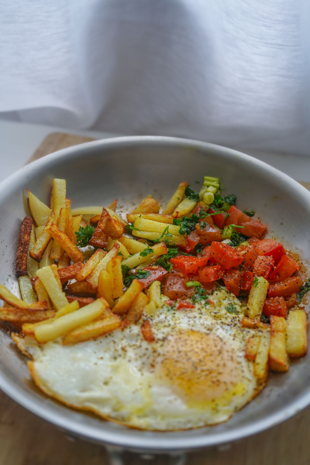 A savory breakfast skillet featuring a fried egg, golden fries, and fresh salad garnished with herbs.
