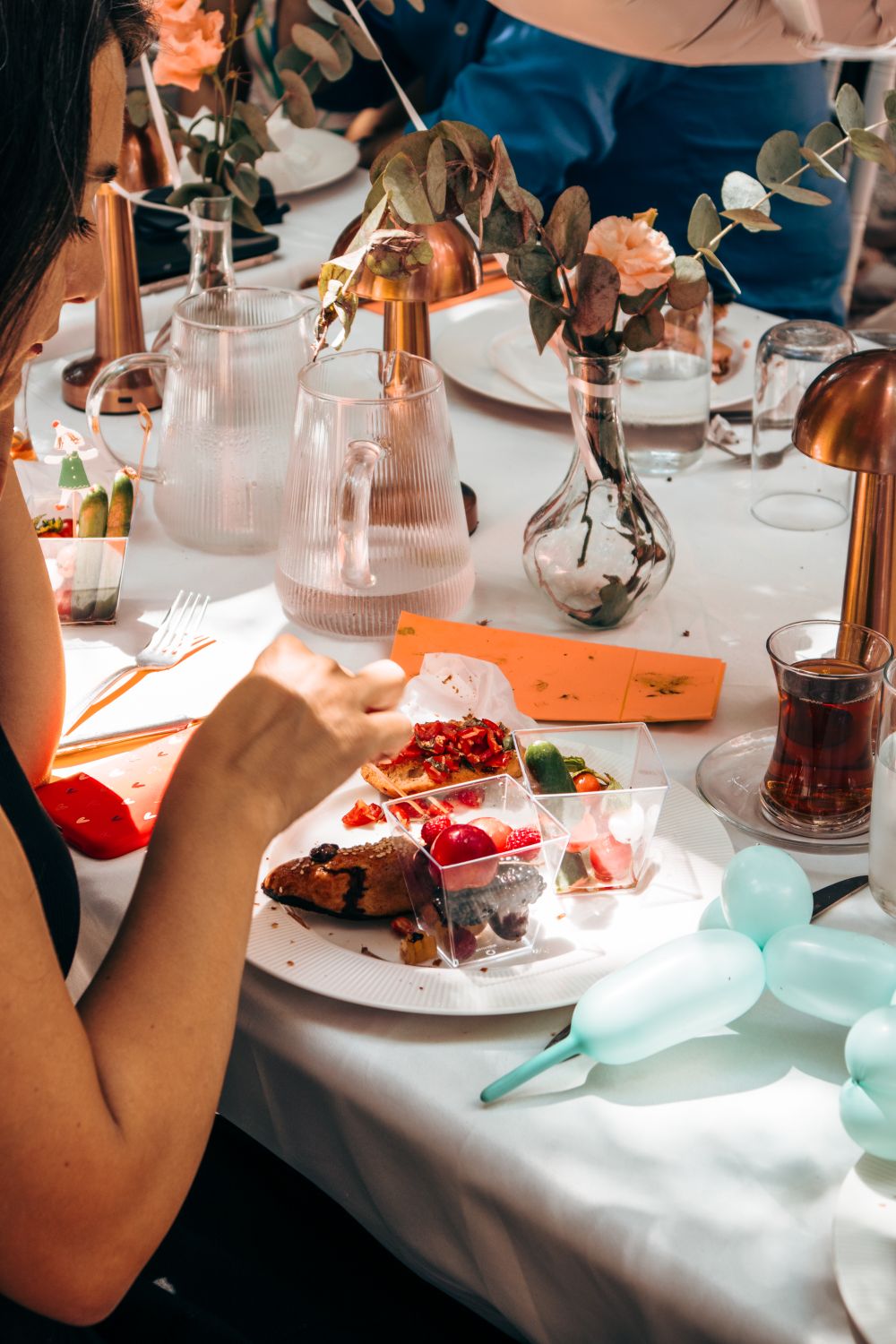 A vibrant, sunlit outdoor dining scene with elegant table settings, floral decor, and delicious food.