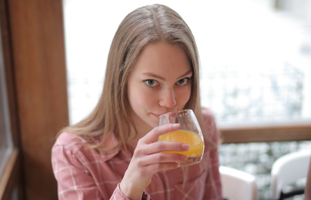 A young woman in a cozy indoor setting sips fresh orange juice, enjoying a relaxed moment.
