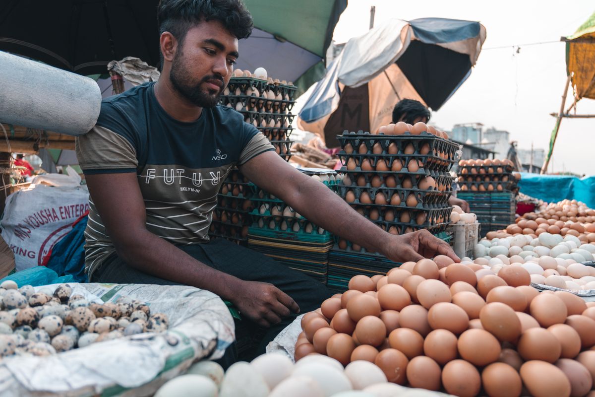 Asian vendor arranging stacks of eggs at a bustling outdoor market.