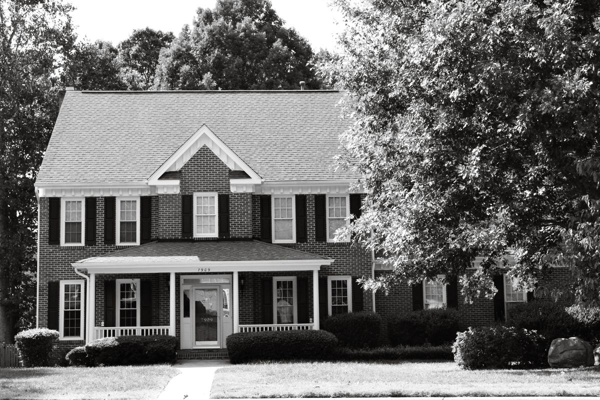 Black and white photo of a colonial brick house surrounded by trees in North Carolina.