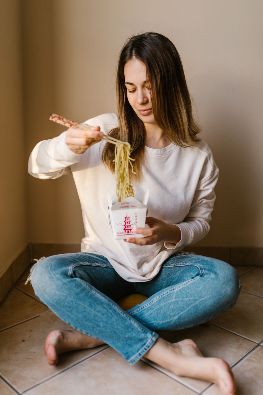 Casual portrait of a young woman eating noodles with chopsticks in a cozy indoor setting.