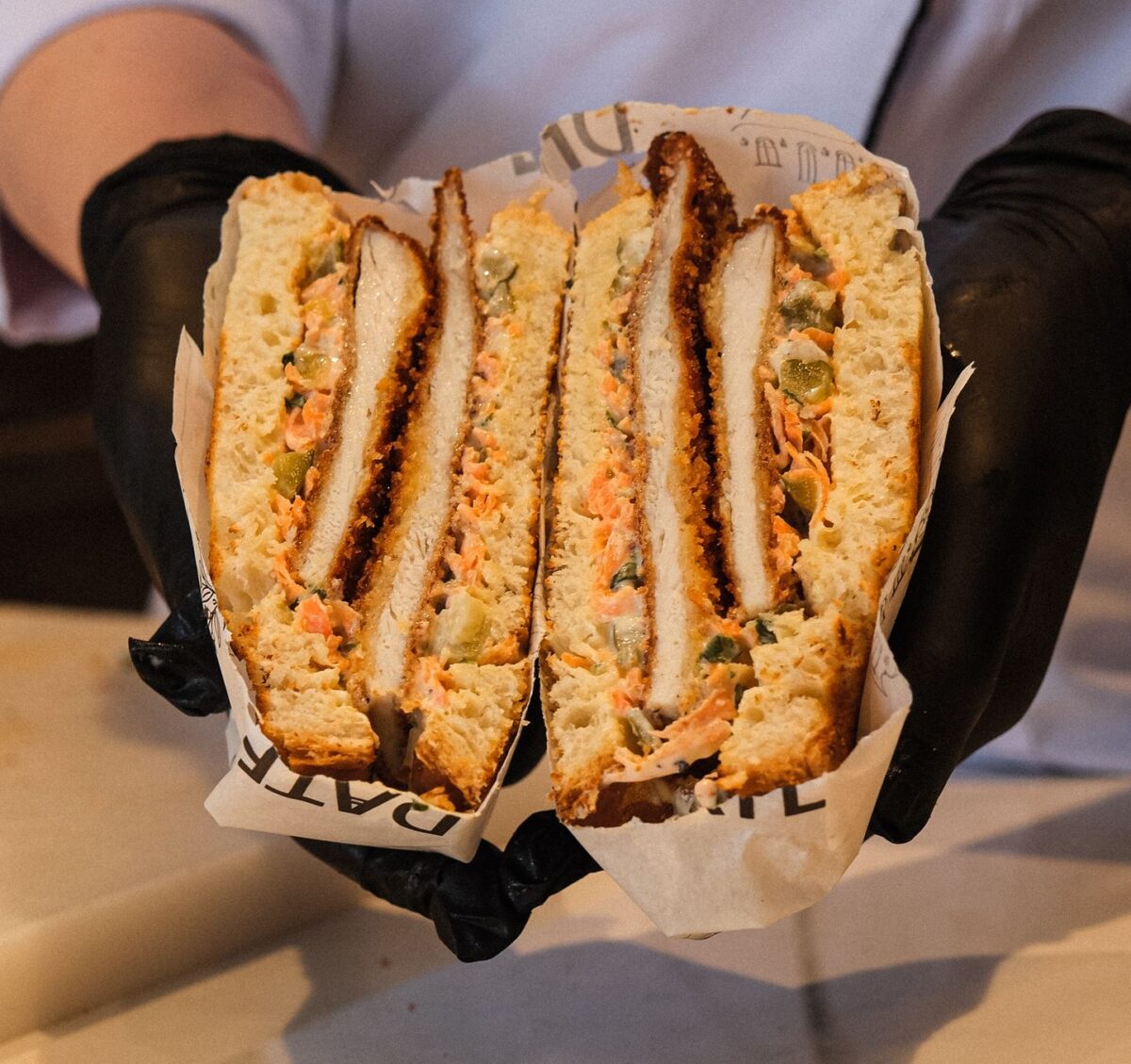 Chef presenting a delicious homemade chicken sandwich cut in half, showcasing fresh ingredients.