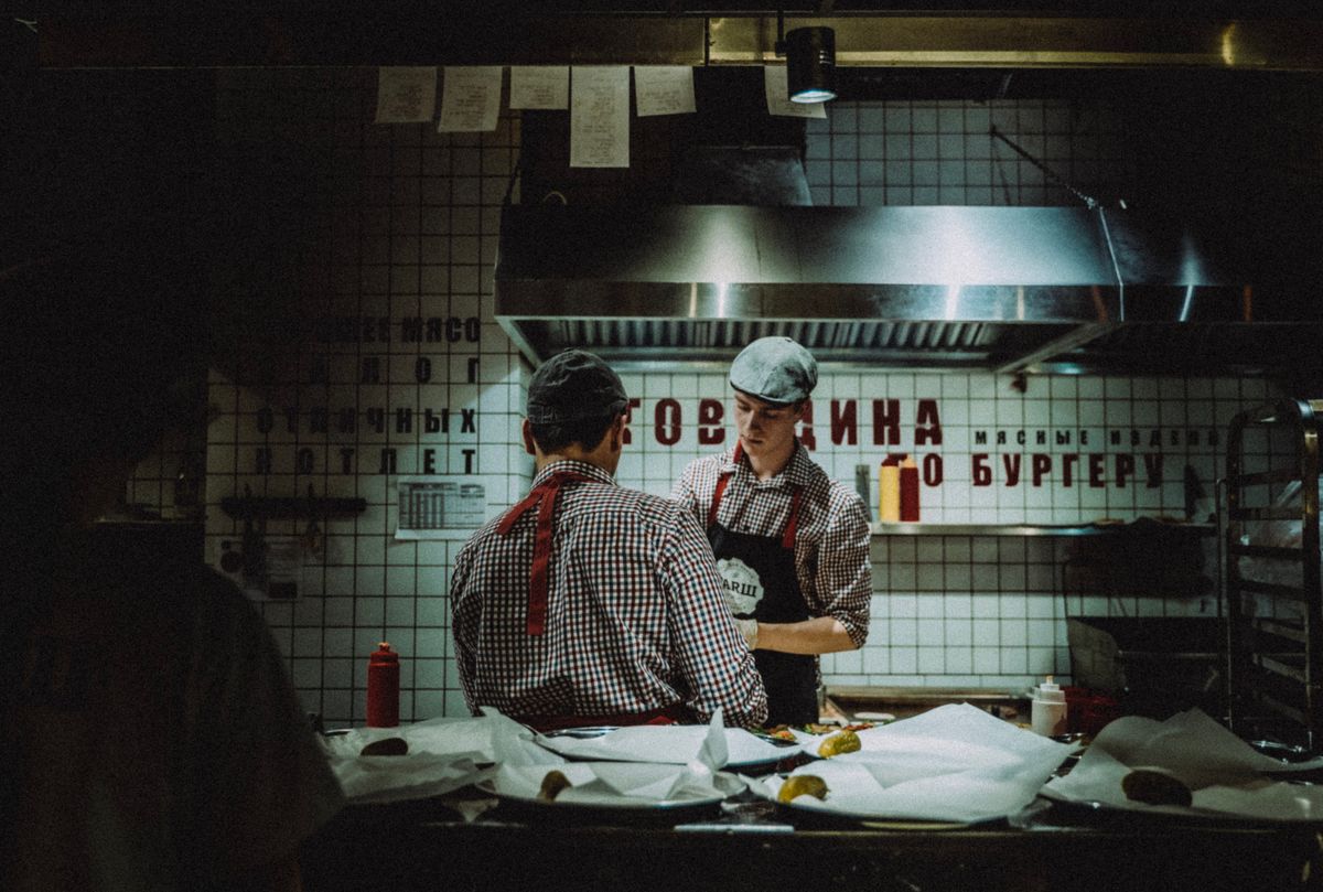 8 Restaurant Secrets That Make Professional Kitchens Run Better Than Most Home Cooks Realize 1 Chefs working in dimly lit kitchen, preparing food. Atmosphere is rustic and industrial.