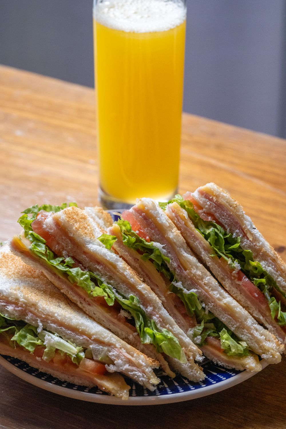 Close-up of a BLT sandwich with lettuce, tomato, and bacon served with orange juice.