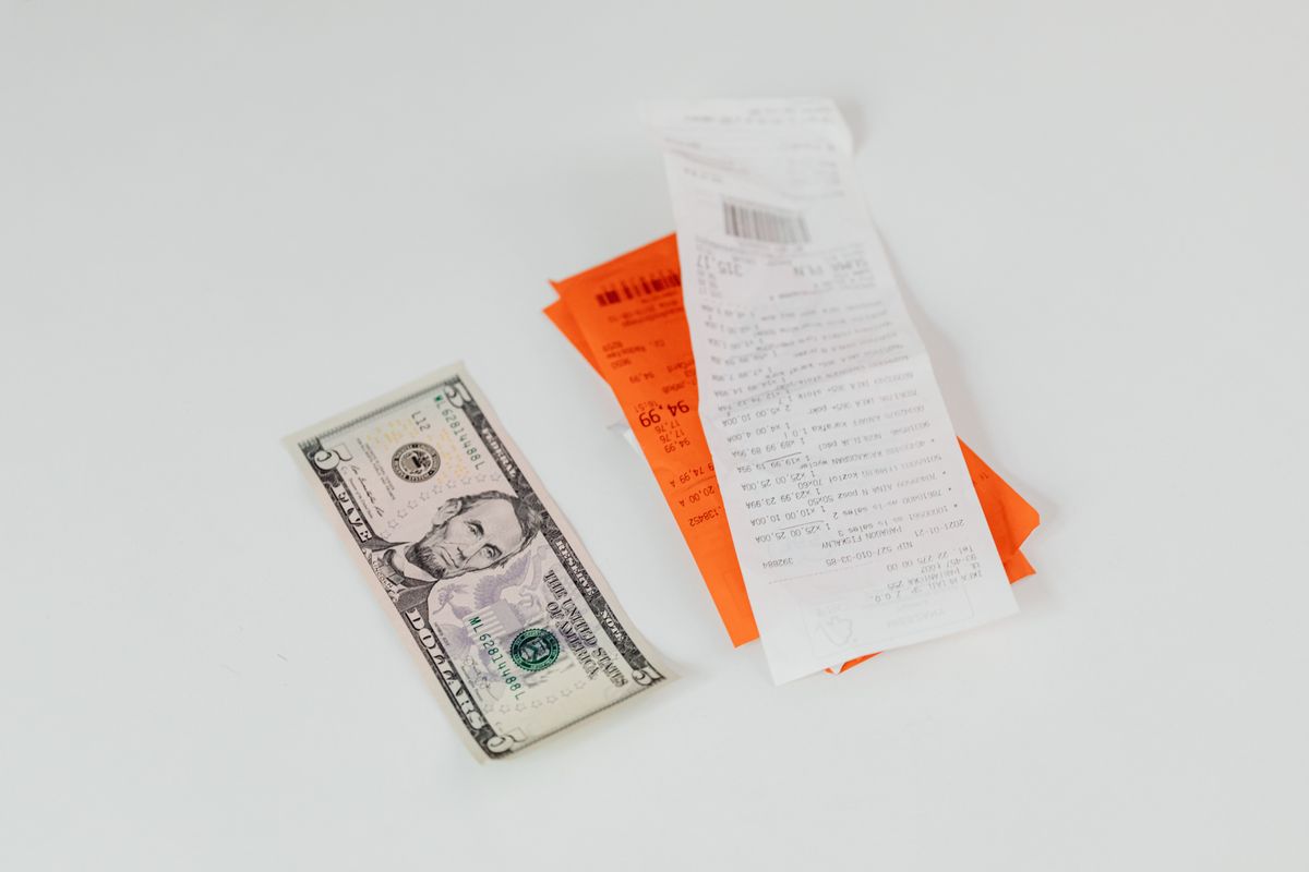 Close-up of a five-dollar bill next to shopping receipts on a white background, ideal for finance and retail themes.