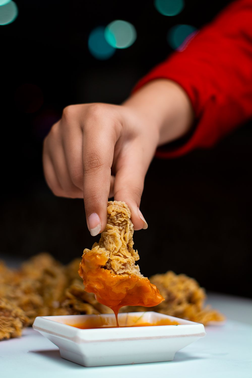 Close-up of a hand dipping a piece of crispy fried chicken into sauce, showcasing texture and deliciousness.
