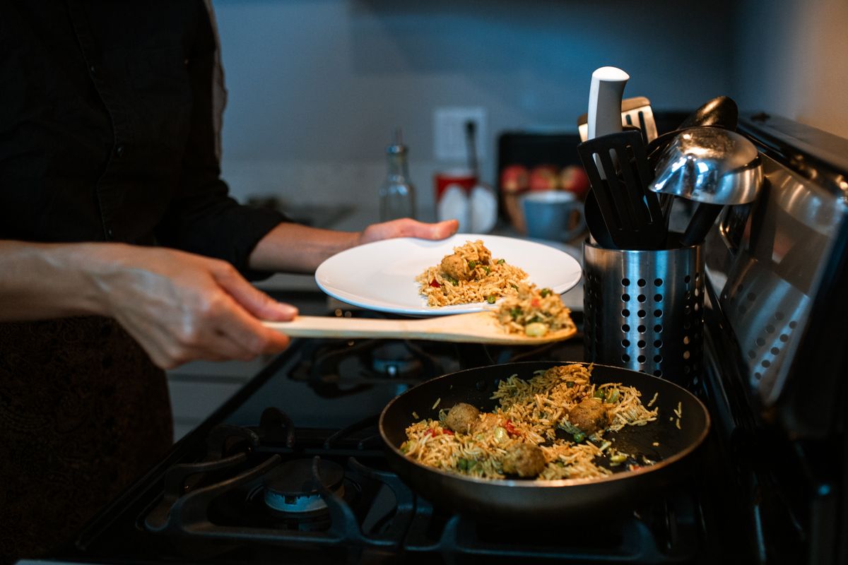 Close-up of a person serving delicious home-cooked fried rice from a pan in a kitchen setting.