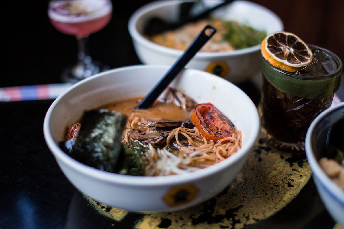 Close-up of a savory ramen bowl featuring noodles, roasted vegetables, and soup in a cozy setting.