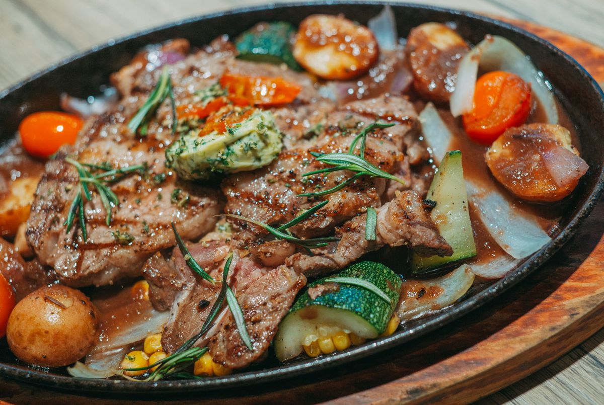 Close-up of a sizzling steak platter with fresh vegetables on a wooden table.