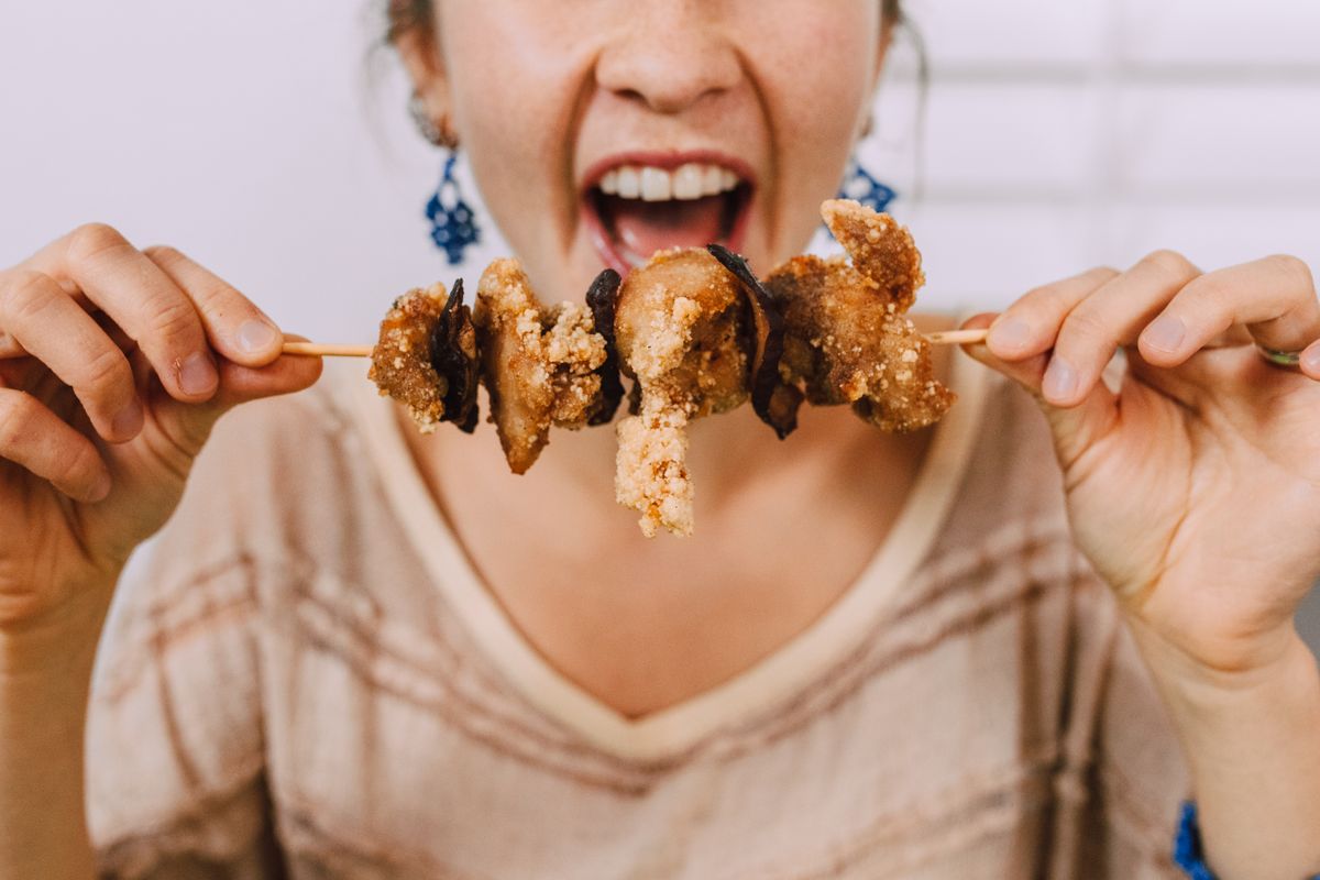 Close-up of a woman about to eat a skewer with delicious crispy Asian food.