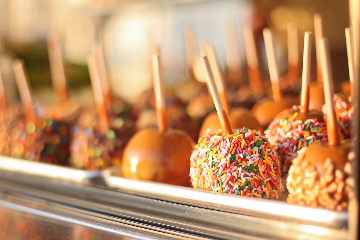 Close-up of caramel apples with colorful sprinkles in vibrant lighting highlights taste appeal.