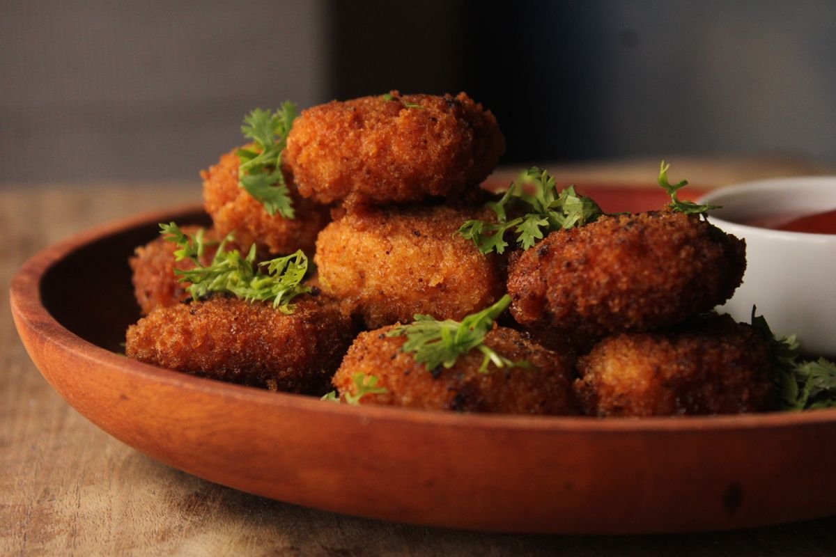 Close-up of crispy croquettes garnished with herbs, served with a side of sauce.