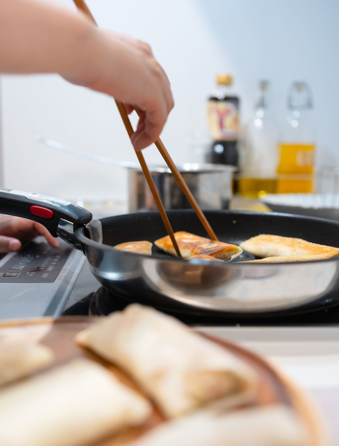 Close-up of dumplings being cooked in a pan using chopsticks in a modern kitchen setting.