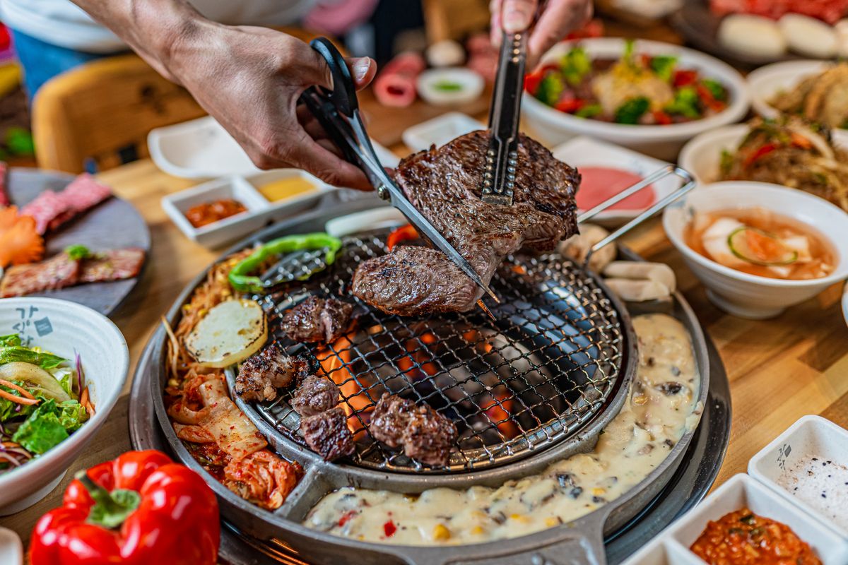 Close-up of grilling beef with scissors at a vibrant Korean BBQ dinner table.