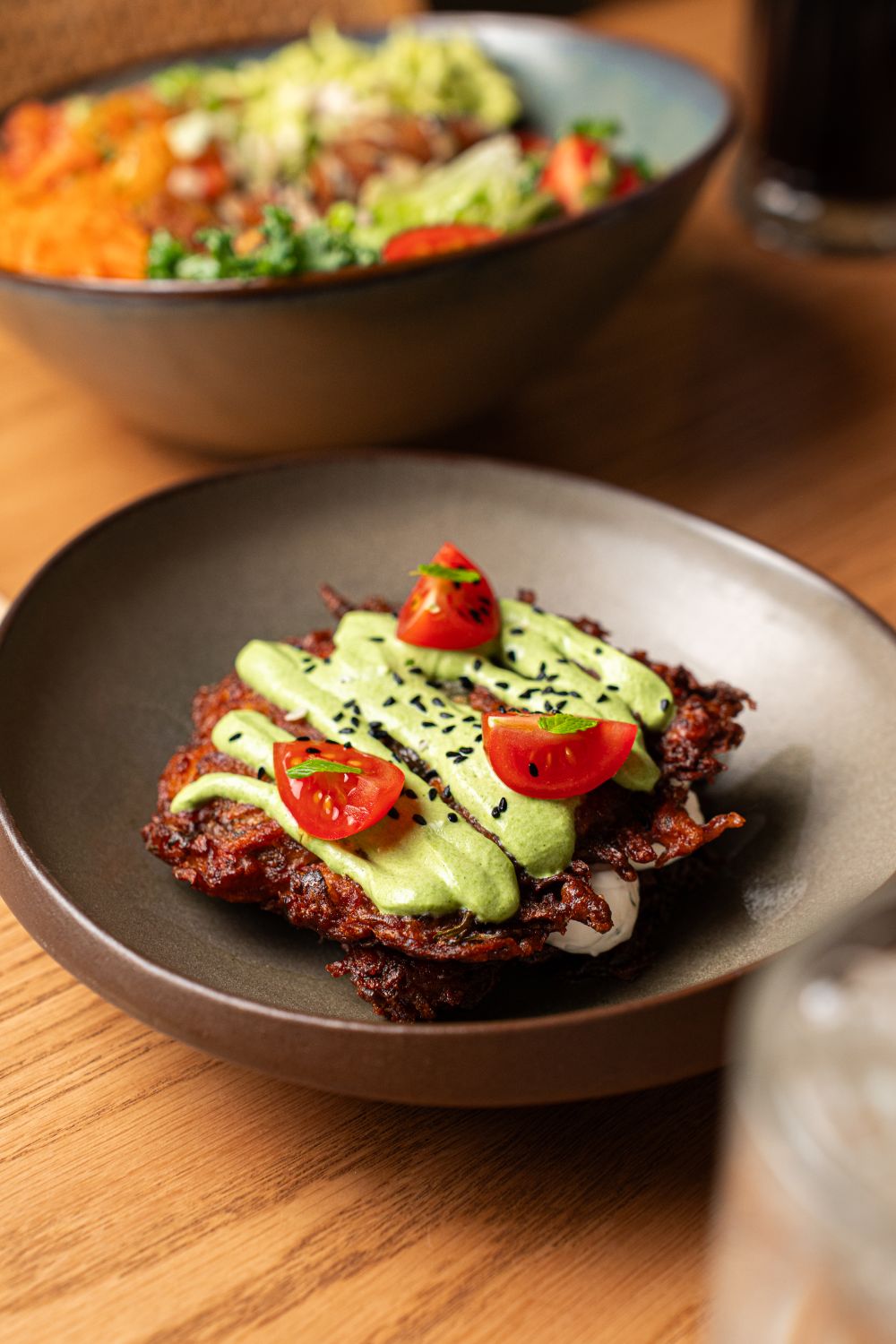 Close-up of mücver topped with avocado cream and fresh tomatoes, garnished with black sesame seeds.