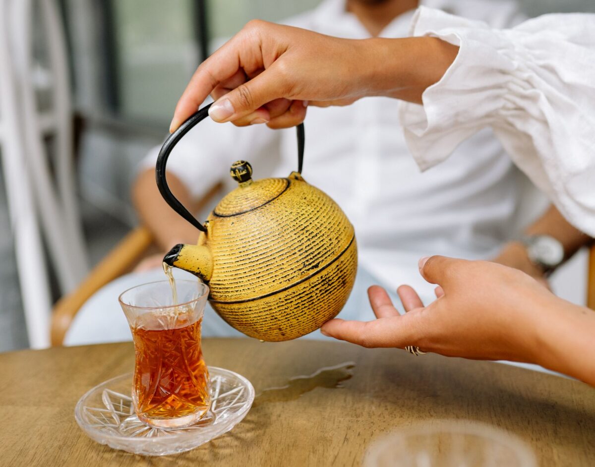 Close-up of pouring tea into a glass cup with a smiling person in the background.