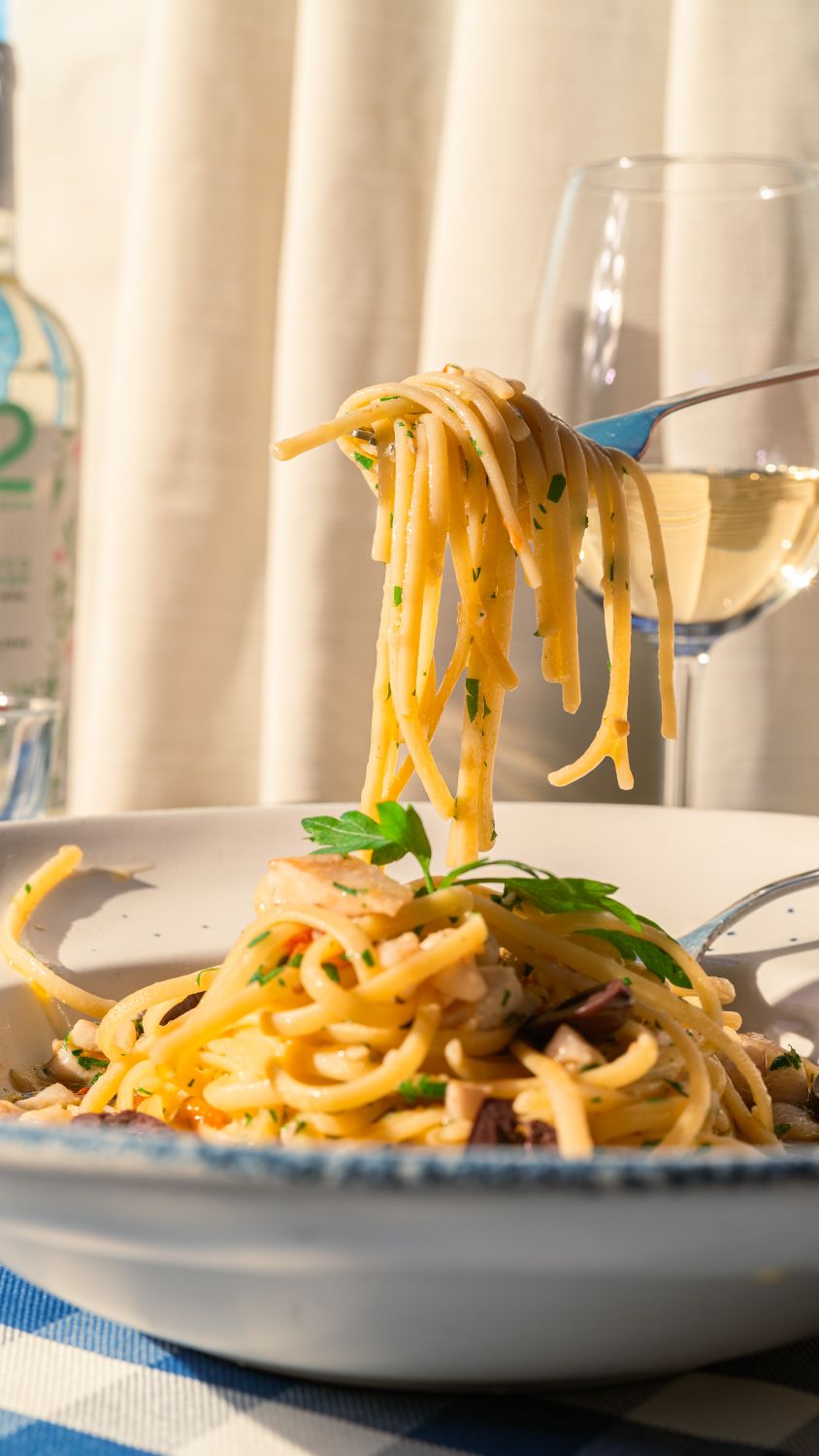 Close-up of spaghetti pasta with herbs, paired with white wine, in an elegant dining setting.