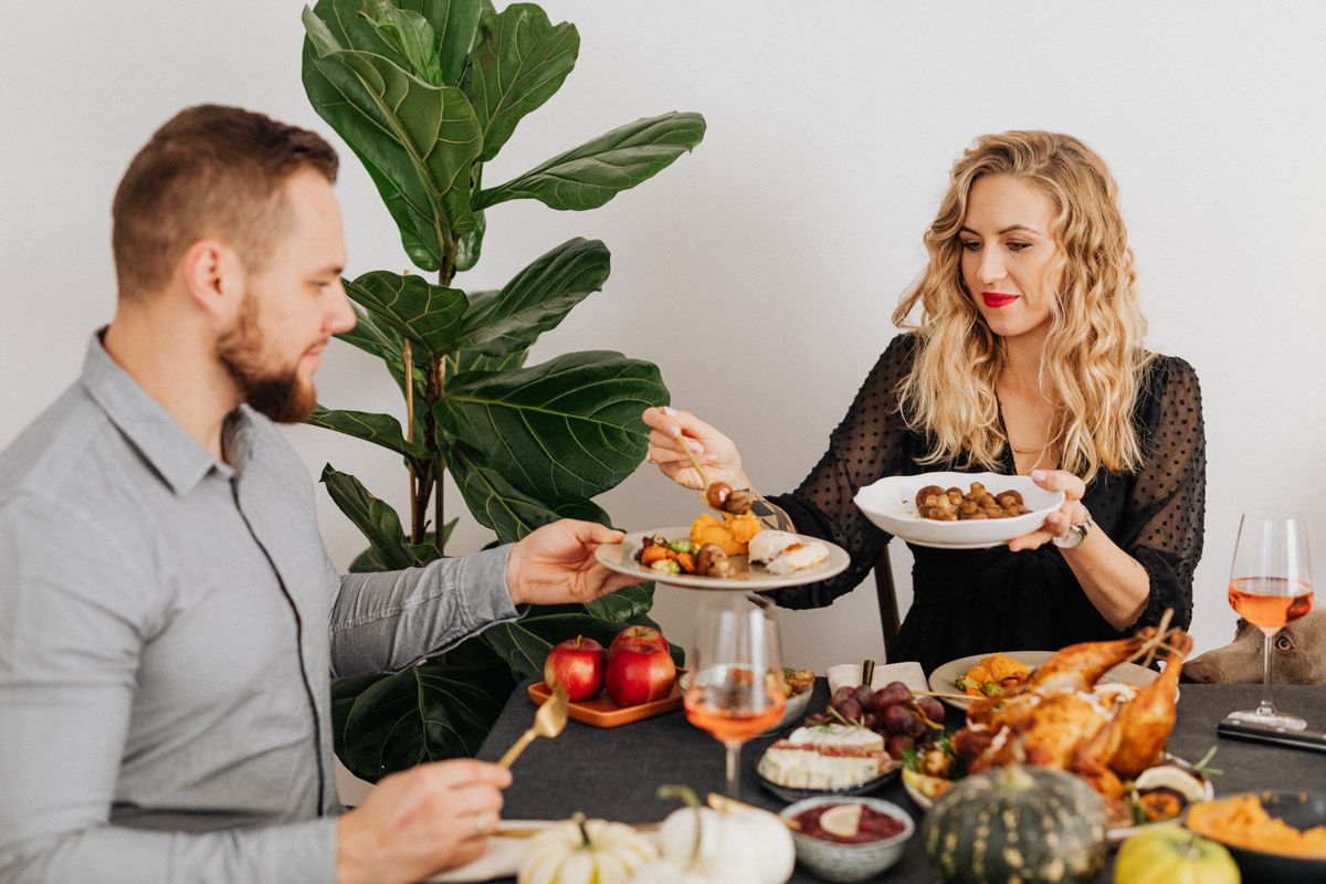 Couple enjoying a delicious Thanksgiving dinner indoors, sharing dishes at a warmly set table.