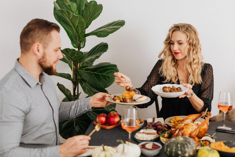 Couple enjoying a delicious Thanksgiving dinner indoors, sharing dishes at a warmly set table.